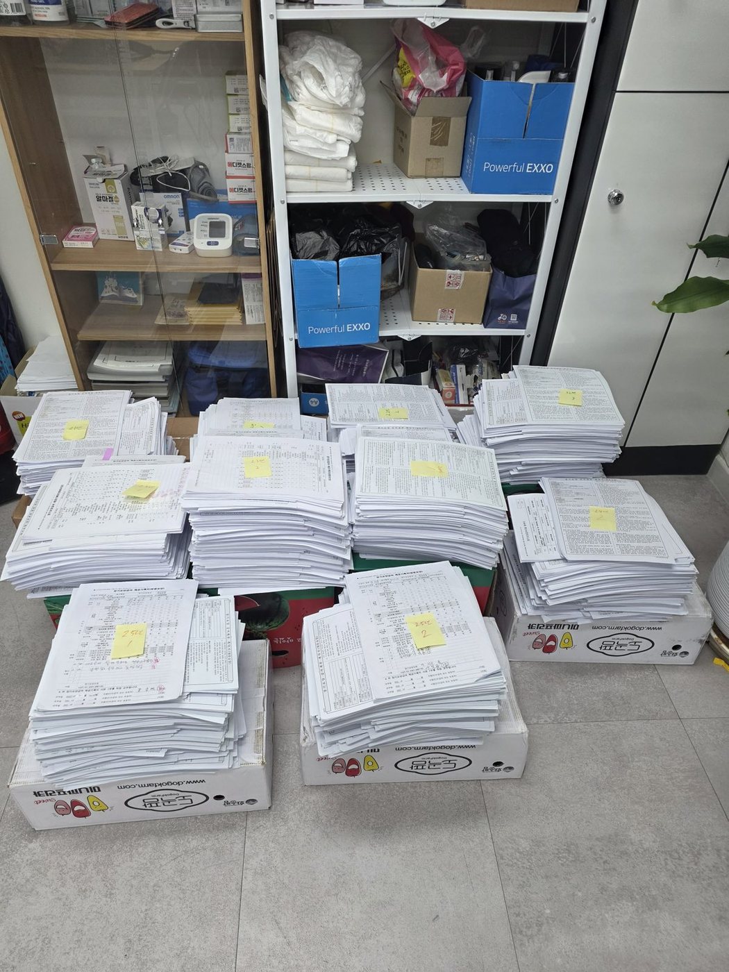 방문요양 사무실 바닥에 급여제공기록지 묶음을 색인 메모와 함께 여러 더미로 쌓아 놓은 모습